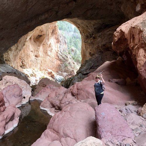 A person stands in a rocky cave with a river flowing beneath, surrounded by colorful rock formations.