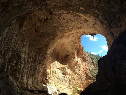 A large cave opening reveals a bright blue sky and rugged rock formations inside the cave.