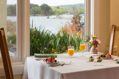 A dining table set with two glasses of orange juice, plates of food, and a vase of flowers, overlooking a scenic lake view.