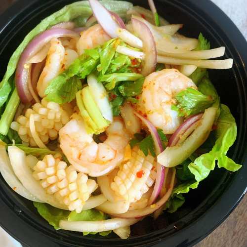 A bowl of shrimp and squid salad with lettuce, onions, and herbs, drizzled with a spicy dressing.