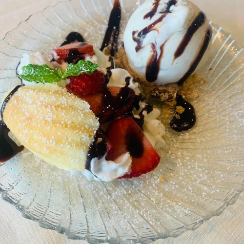 A dessert plate featuring a sponge cake, strawberries, whipped cream, and a scoop of ice cream drizzled with chocolate sauce.
