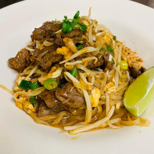 A plate of stir-fried beef with bean sprouts, green onions, and lime, garnished with herbs.
