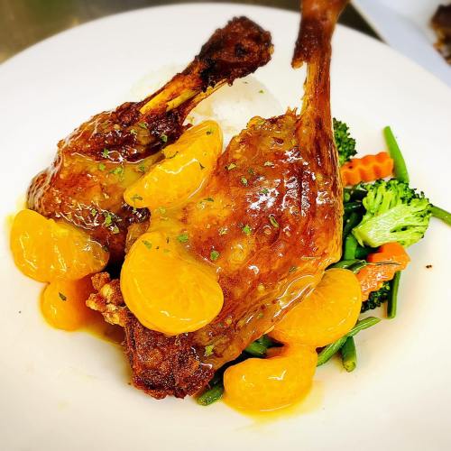 Two crispy chicken legs topped with orange slices, served on a bed of mixed vegetables and rice.