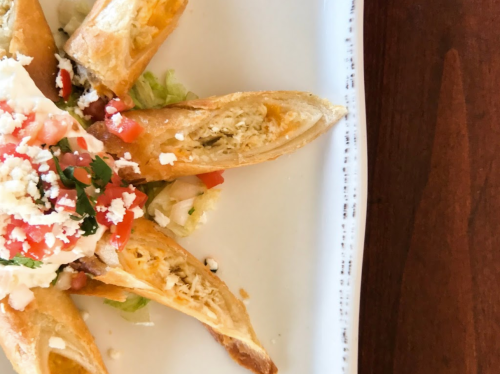 Golden-brown pastry filled with chicken, topped with diced tomatoes, lettuce, and cheese on a white plate.