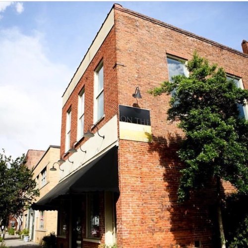 A brick building with large windows and greenery, featuring a sign that reads "ON THE."