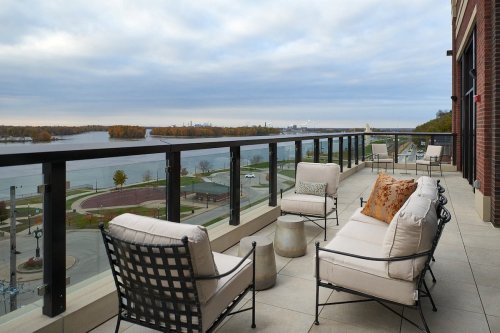 A spacious balcony with stylish seating overlooks a river and autumn trees under a cloudy sky.