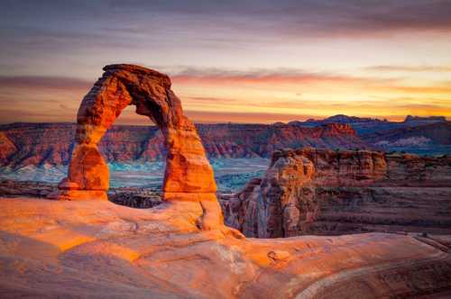 A stunning sunset view of Delicate Arch in Arches National Park, highlighting its natural rock formation and surrounding landscape.