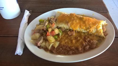 A plate of enchiladas topped with cheese, served with a side of mixed vegetables and beans on a wooden table.