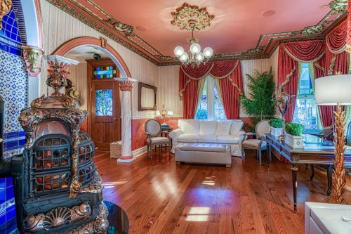Elegant living room with ornate decor, a white sofa, rich drapes, and a vintage stove, featuring warm wooden floors.
