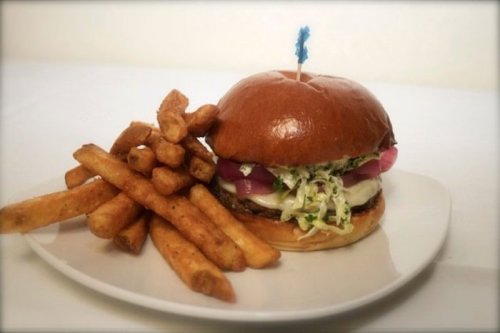 A delicious burger with lettuce, onions, and cheese, served with crispy fries on a white plate.