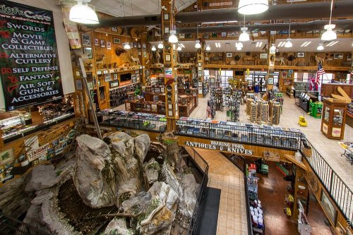 A spacious store interior filled with collectibles, cutlery, and outdoor gear, featuring a rock fountain in the center.