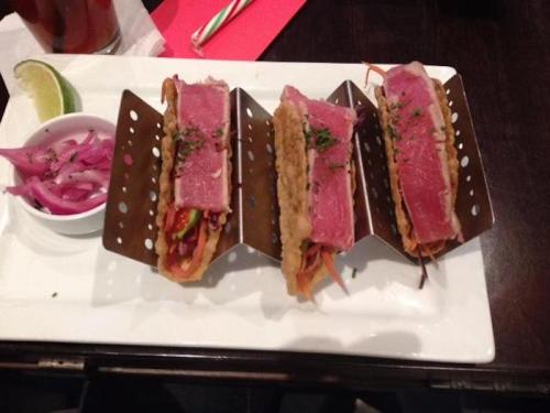 Three tacos with tuna, served on a white plate with pickled onions and a lime wedge on the side.