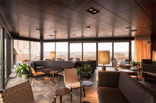 A modern lounge with large windows, stylish seating, plants, and warm lighting, offering a cozy atmosphere.