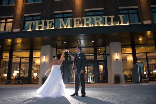 A couple dances joyfully outside The Merrill, illuminated by warm lights in the evening.
