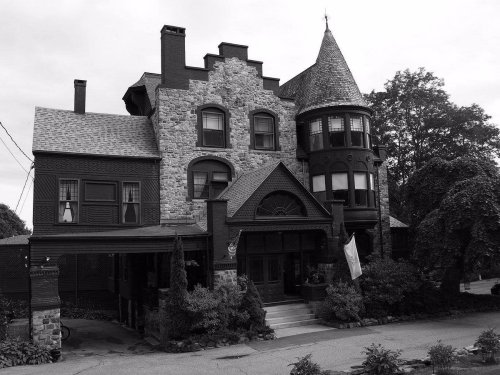 A large, historic house with stone and wood features, a turret, and a steep roof, surrounded by greenery.