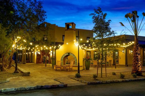 A charming outdoor patio with string lights, a fireplace, and desert landscaping under a twilight sky.