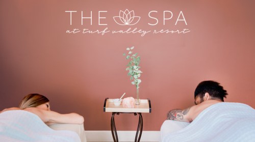 Two people receiving massages at The Spa, Turf Valley Resort, with a calming decor and a small table between them.