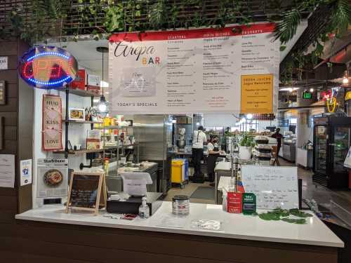 A vibrant food stall with a menu board, open sign, and kitchen area, featuring arepas and daily specials.