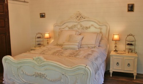 A cozy bedroom featuring a vintage white bed, soft bedding, and warm lamps on nightstands.