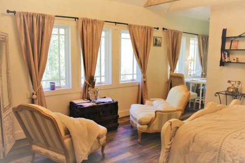 Cozy room with two armchairs, large windows, and soft curtains, featuring a small table and decorative shelves.