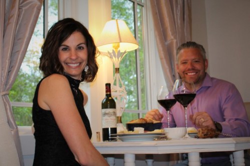 A couple enjoys a romantic dinner with wine, bread, and a cozy setting by a window.