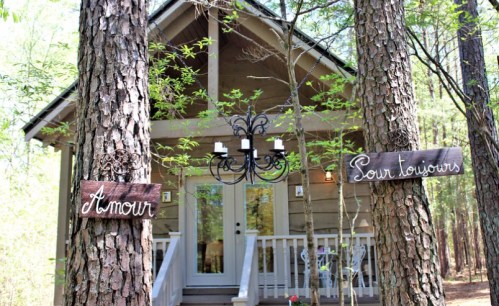 A cozy cabin nestled among trees, with signs reading "Amour" and "Pour toujours" hanging from the trunks.