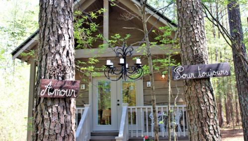 A cozy cabin nestled among trees, with signs reading "Amour" and "Pour toujours" on either side of the entrance.