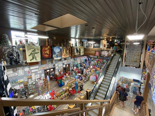 A bustling gift shop with colorful merchandise, art displays, and shoppers on multiple levels. Brightly lit and inviting atmosphere.