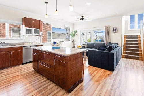 Modern kitchen with an island, stainless steel appliances, and a cozy living area featuring a sofa and staircase.