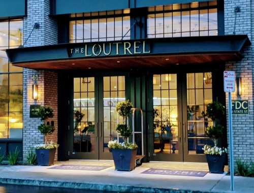 Entrance of The Loutrel hotel featuring large glass doors, potted plants, and a welcoming atmosphere.