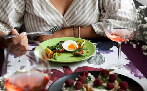 A person holds a fork near a green plate with a salad and a soft-boiled egg, with glasses of rosé wine in the foreground.