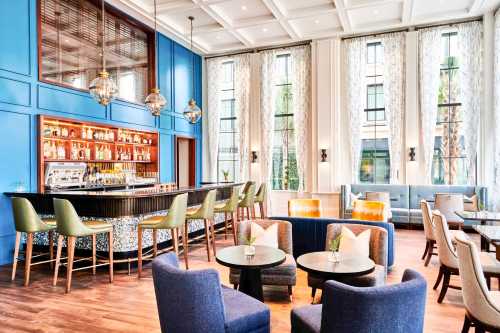 Stylish bar area with blue walls, modern seating, and large windows, featuring a well-stocked bar and elegant decor.