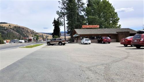 A small restaurant building beside a highway, with several parked cars and trees in the background.