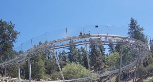 A roller coaster track winds through trees under a clear blue sky, with a cart at the top of a loop.
