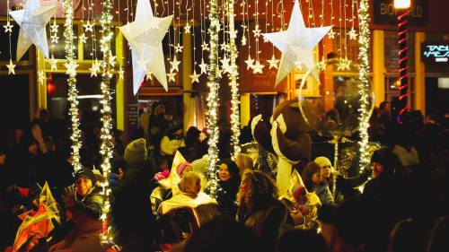 A festive scene with illuminated stars and lights, featuring a crowd of people enjoying a celebration.
