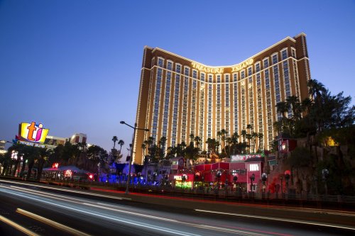 Treasure Island hotel illuminated at dusk, with colorful lights and palm trees lining the street in Las Vegas.
