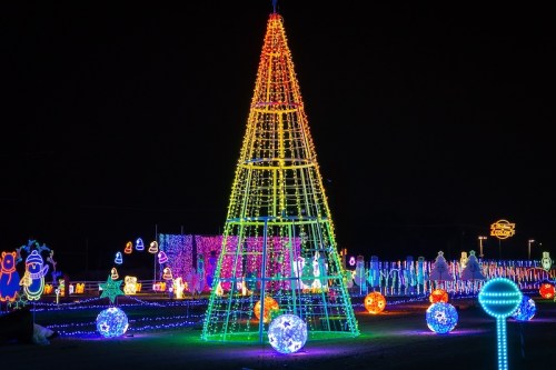 A brightly lit, colorful Christmas tree surrounded by festive light displays at night.