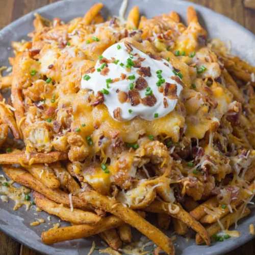 A plate of loaded fries topped with cheese, bacon, sour cream, and chives.