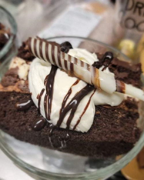 A close-up of a chocolate dessert topped with whipped cream, chocolate drizzle, and a decorative chocolate stick.