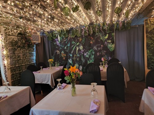 Cozy restaurant interior with tables set for dining, adorned with flowers and twinkling fairy lights.