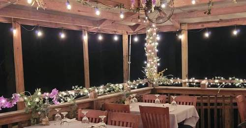 Cozy outdoor dining area with wooden tables, string lights, and floral decorations, creating a warm ambiance.