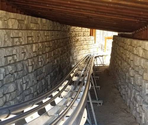 A narrow passageway with stone walls and metal tracks curving through it, partially covered by a wooden structure.