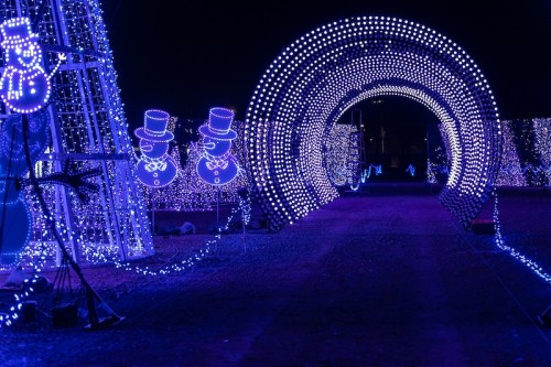 A pathway illuminated with purple lights, featuring snowman decorations and a glowing archway.