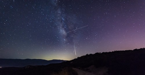 A starry night sky with the Milky Way and a bright meteor streaking across the horizon.