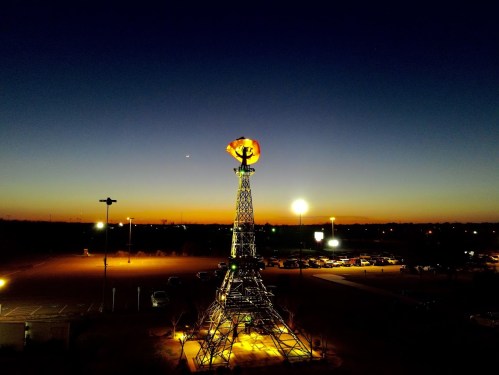 A tall tower with a glowing orb at the top, set against a twilight sky with a fading sunset and distant lights.