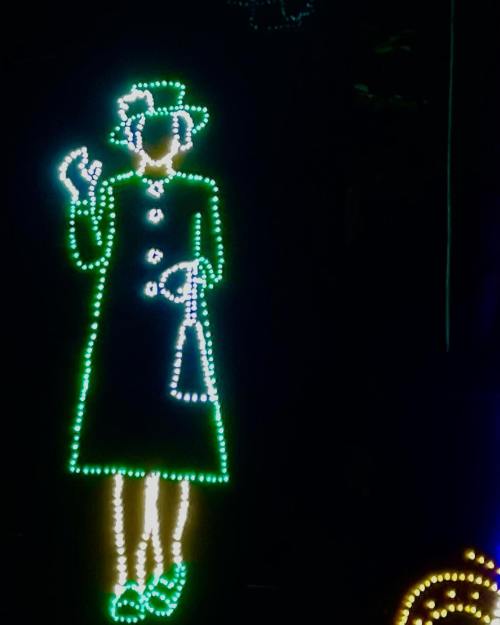 A glowing outline of a person in a green coat and hat, holding a bag, against a dark background.