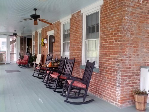 A cozy porch with wooden rocking chairs, brick walls, and ceiling fans, creating a welcoming atmosphere.