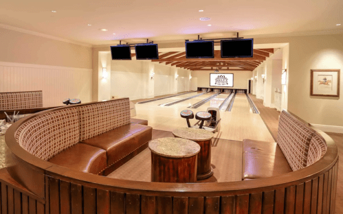 A stylish bowling alley with seating, wooden accents, and multiple screens for entertainment.