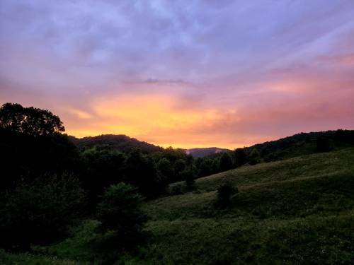 A serene landscape at sunset, featuring rolling hills and a colorful sky with shades of orange and purple.
