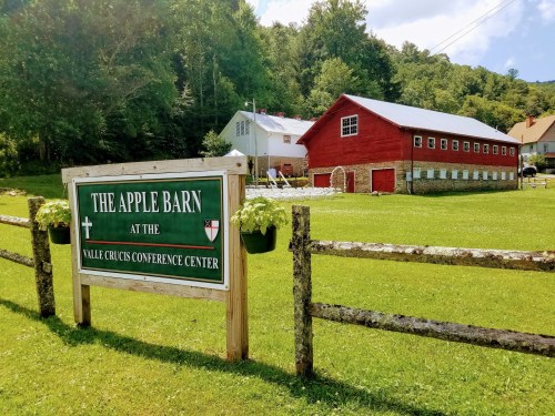 A red barn with a sign reading "The Apple Barn" at a conference center, surrounded by green grass and trees.